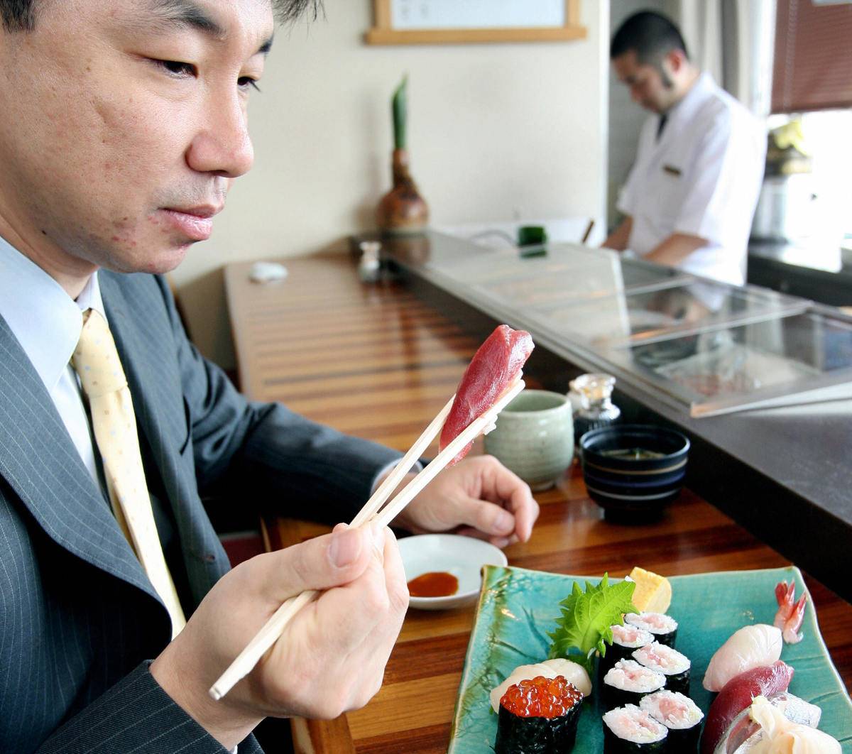 A man picks up raw tuna with chopsticks.
