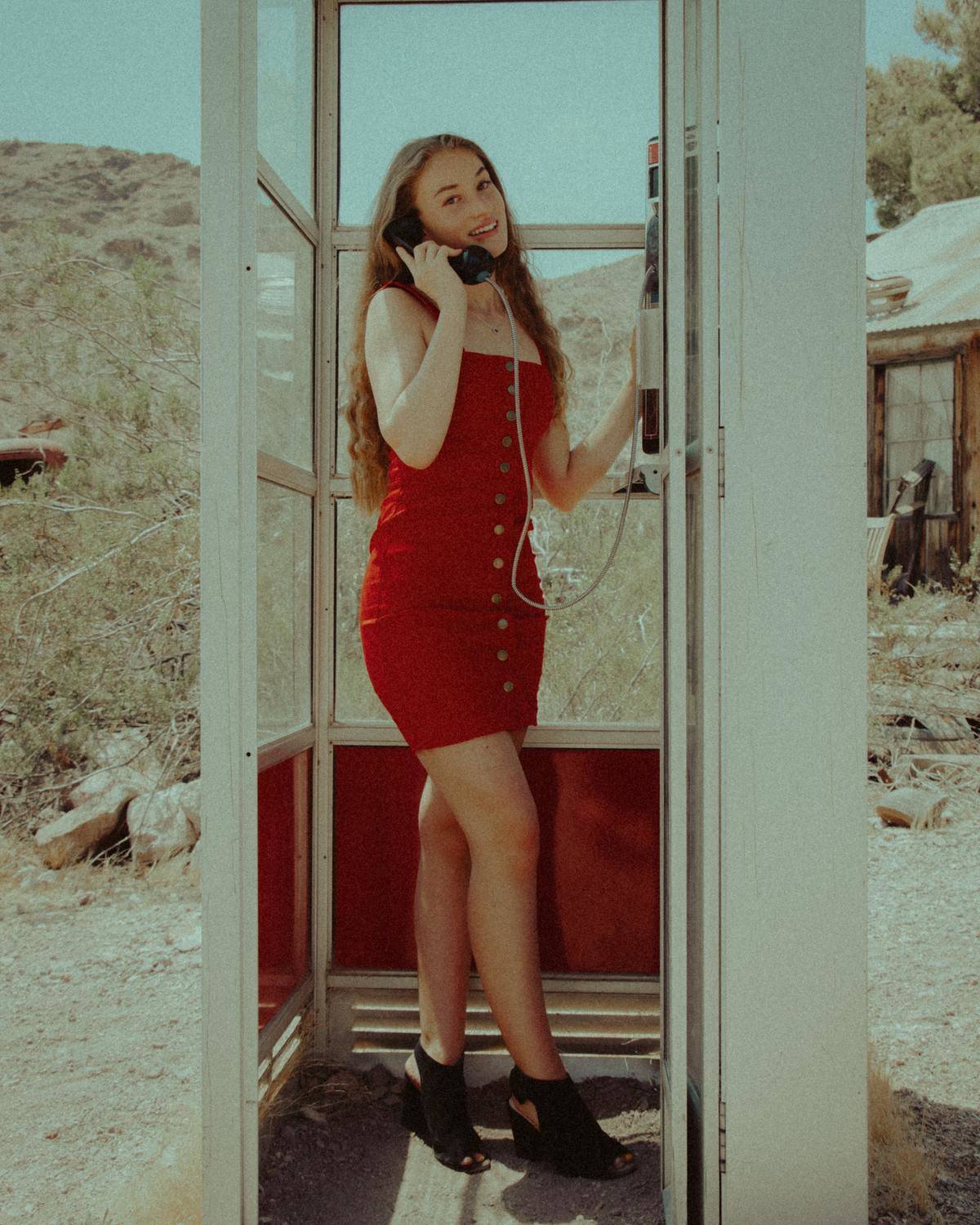 Woman stands in red dress in telephone booth