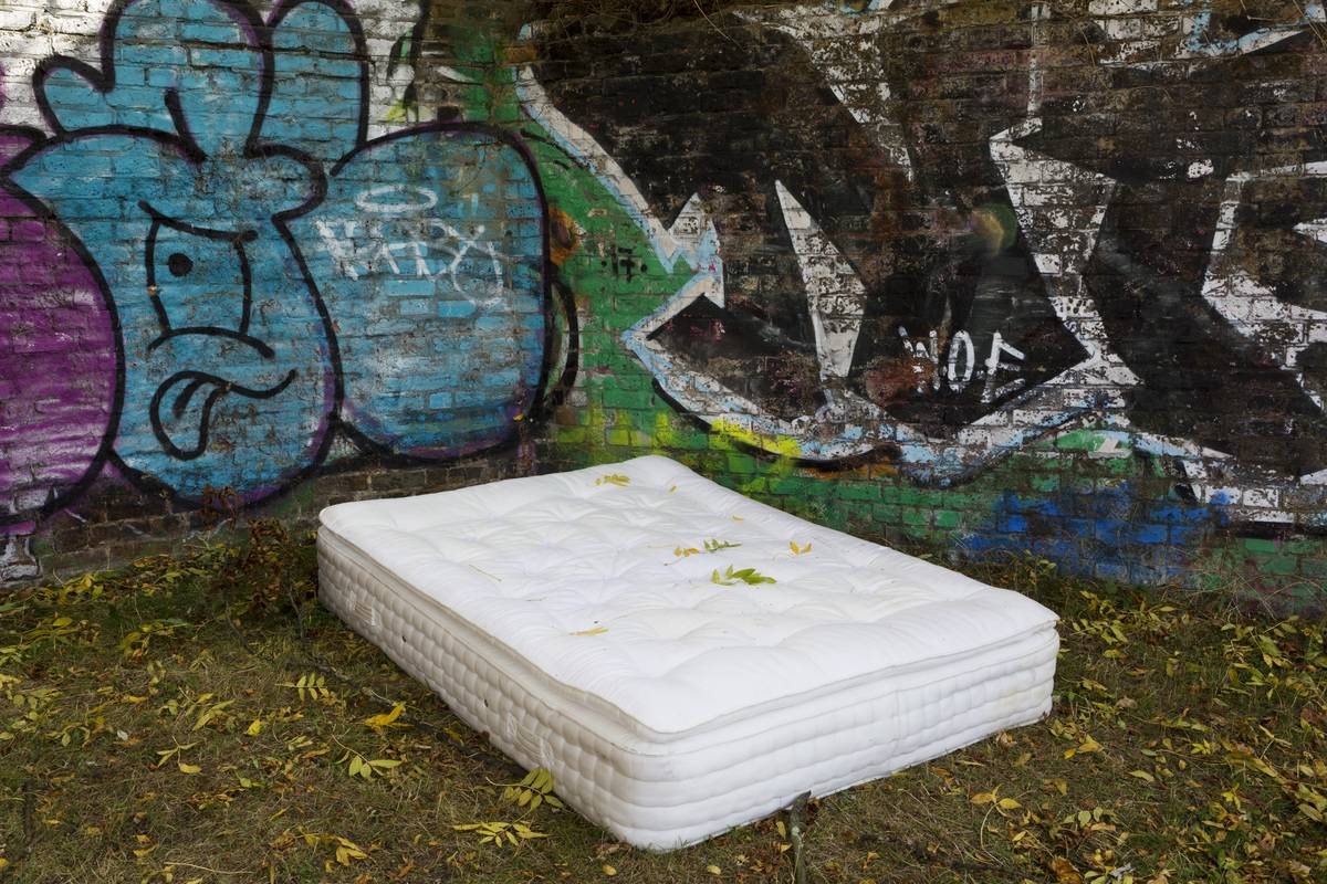 An abandoned mattress lies in front of a graffitied wall.