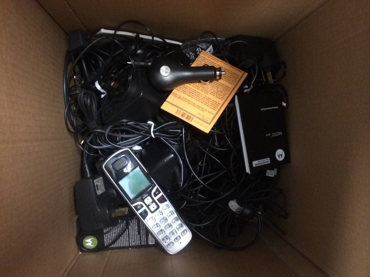 Chargers, cables, and phones lie discarded in a cardboard box.