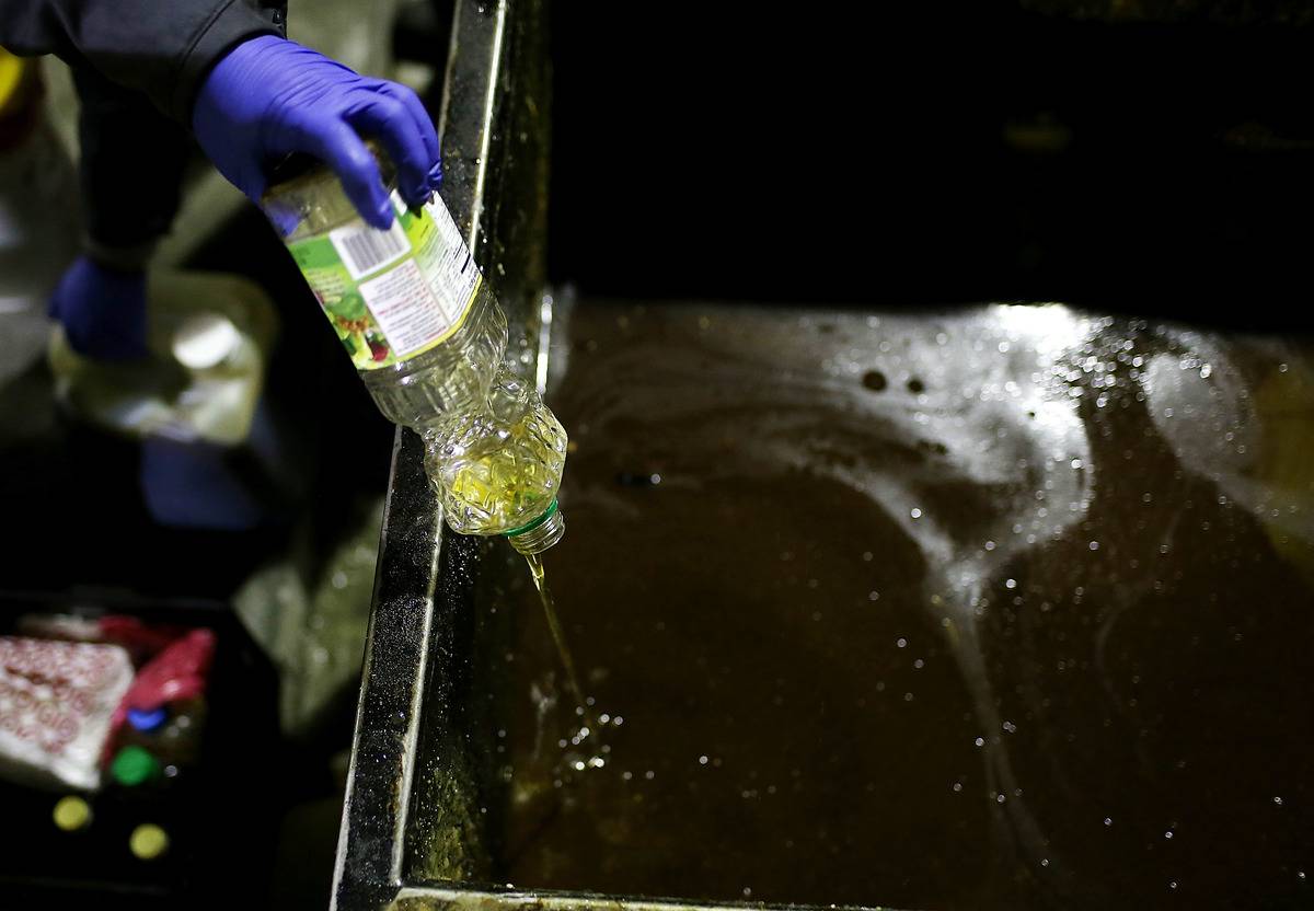 A worker safely disposes of cooking oil.