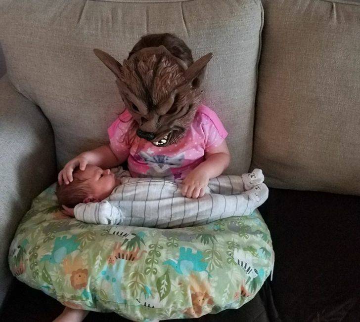 older sister wearing wolf mask to hold baby