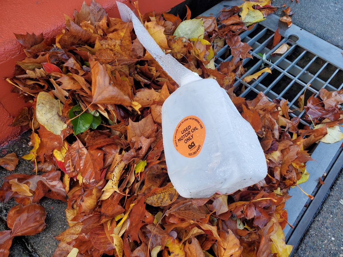 A plastic container of motor oil lies discarded near a storm drain.