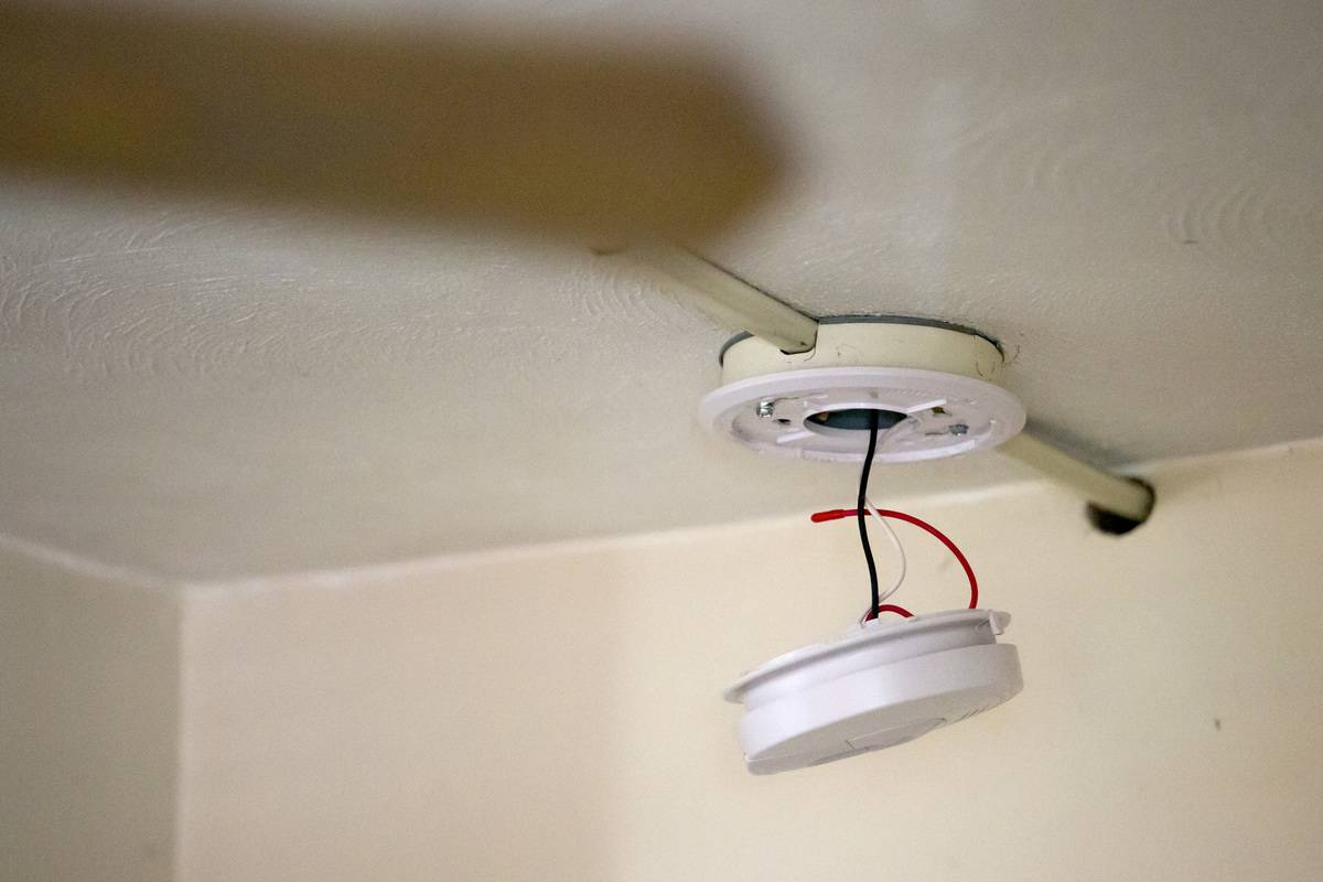 A broken smoke detector hangs from a ceiling.