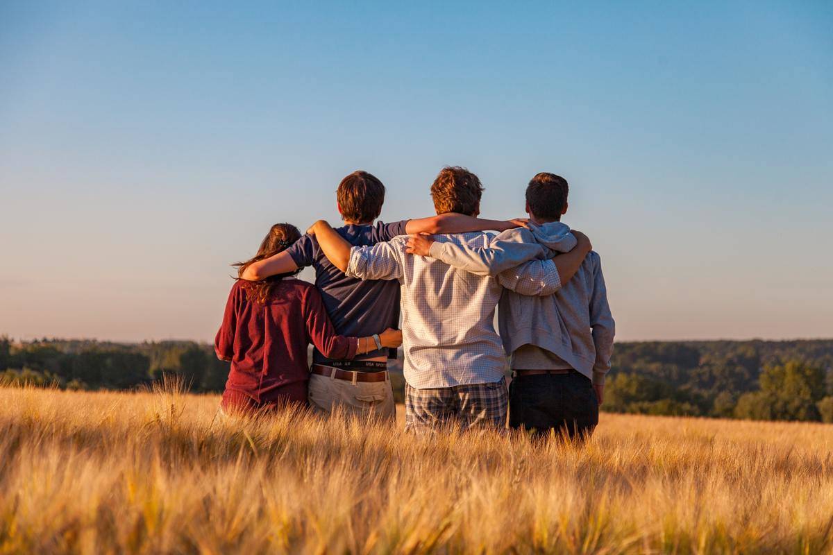 friends embracing facing away in field