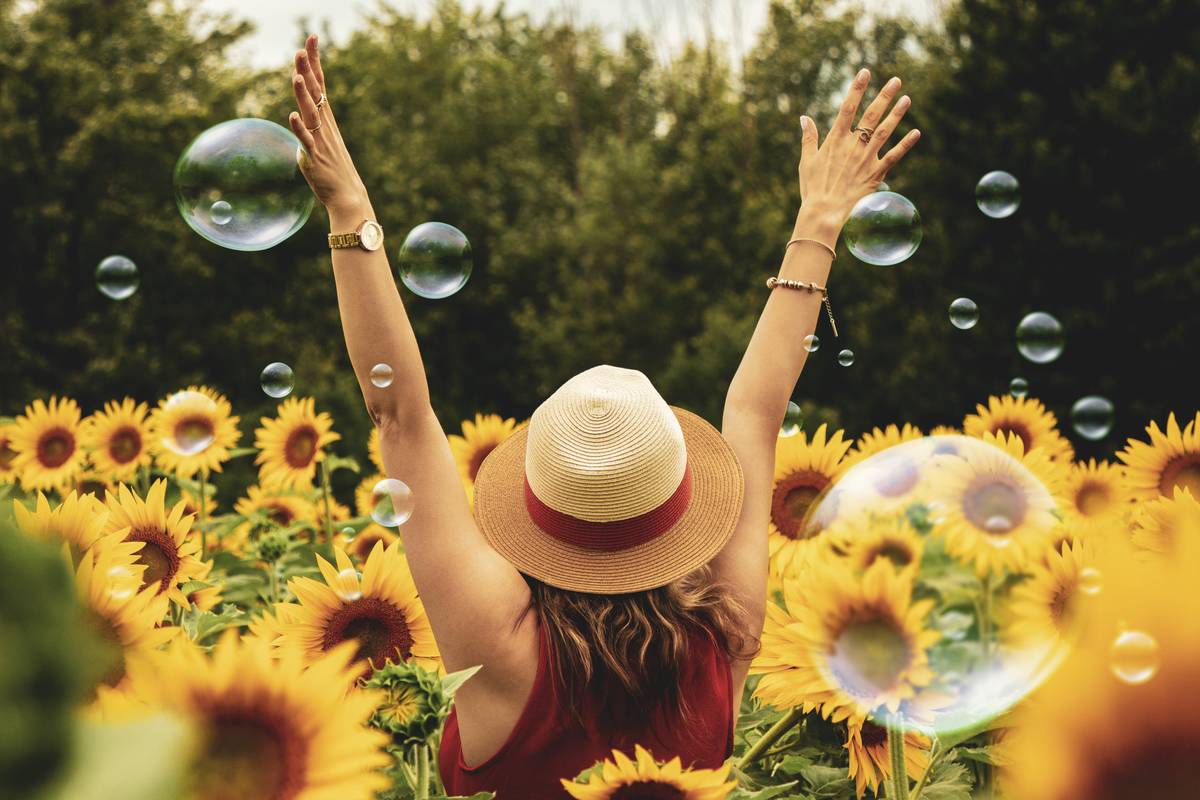 woman standing in field of sunflowers arms raised