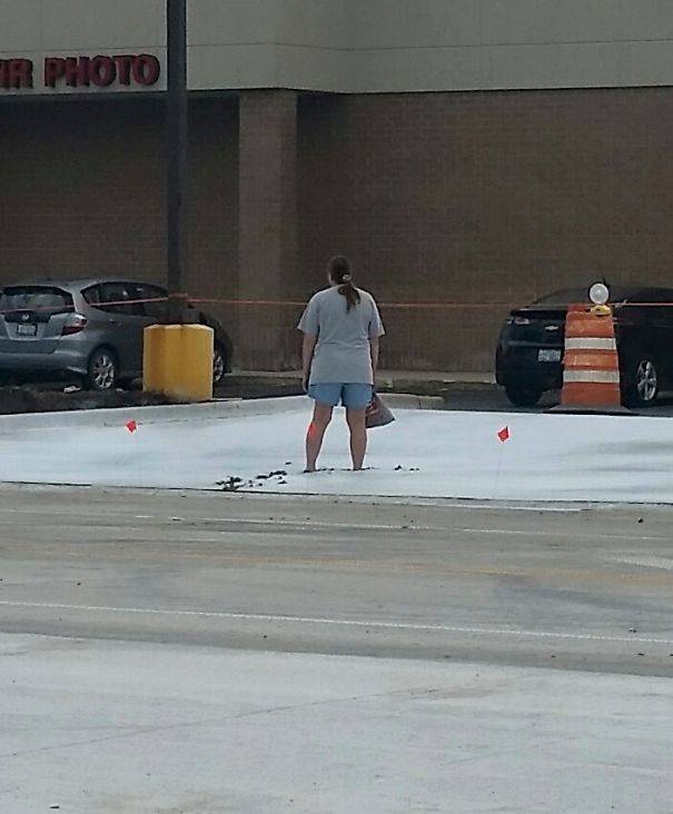 person standing ankle-deep in wet concrete in parking lot.