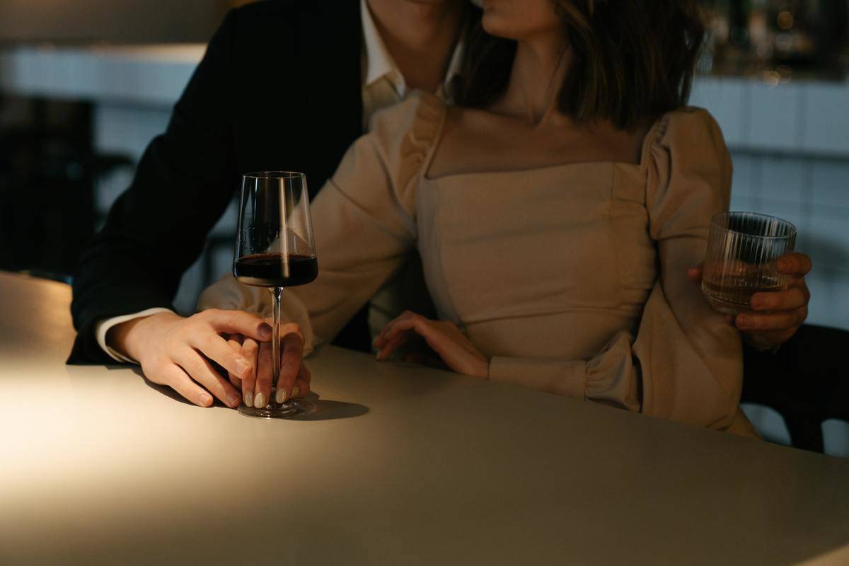 man seated behind woman in bar with glass of wine