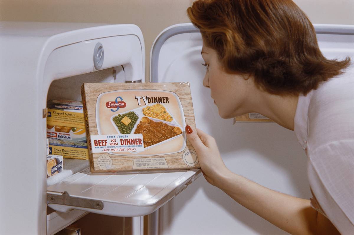 A woman examines a TV dinner box she has taken from the freezer.