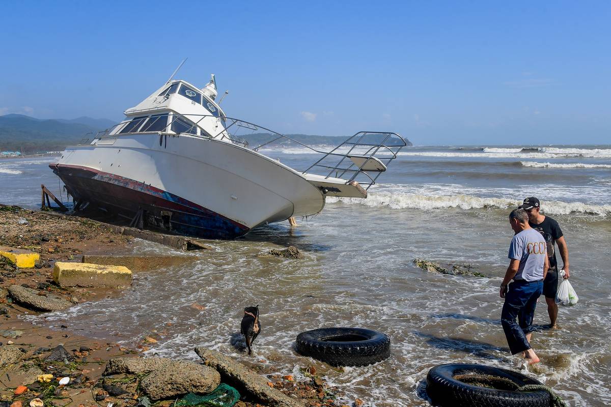 People survey a Russian beach filled with trash and a washed-up boat.