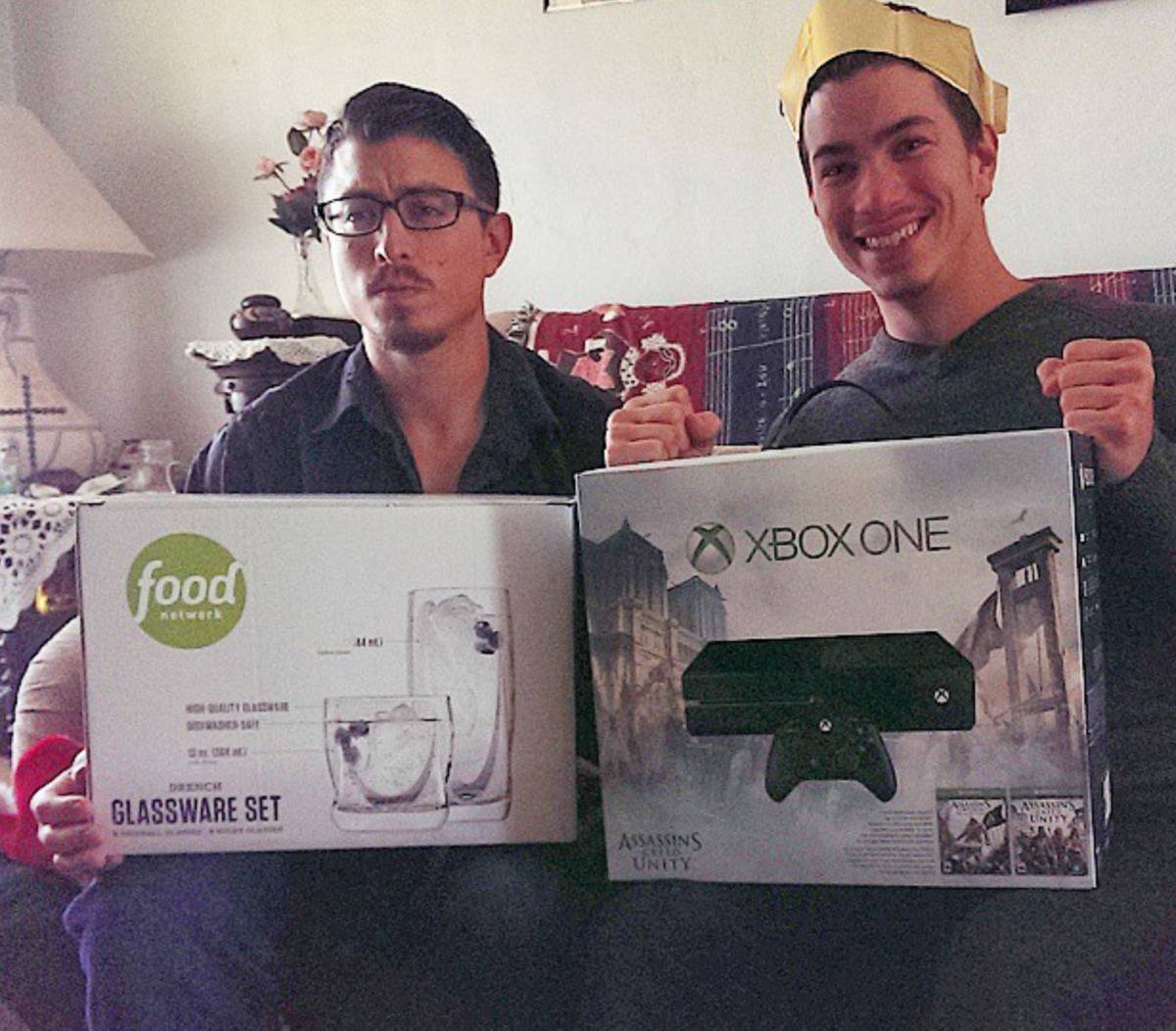 man frowning holding glassware set next to man smiling holding a new xbox