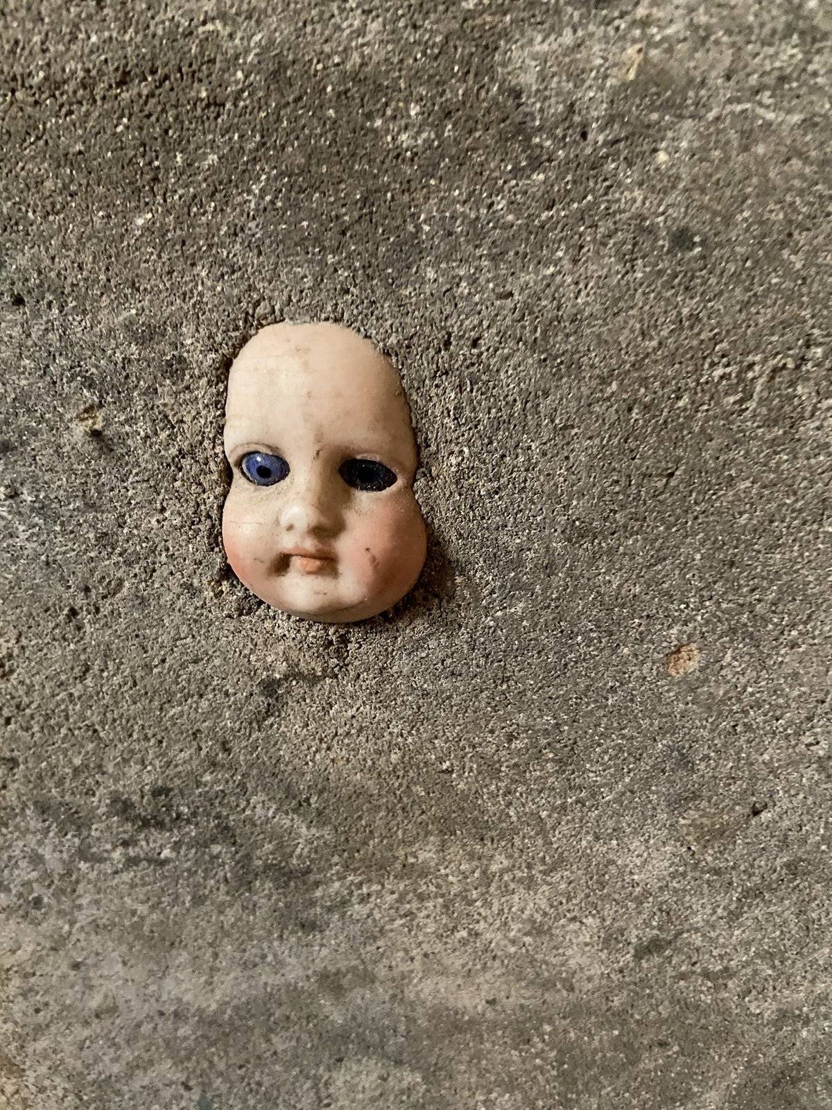A doll baby head peeks out of a concrete wall.