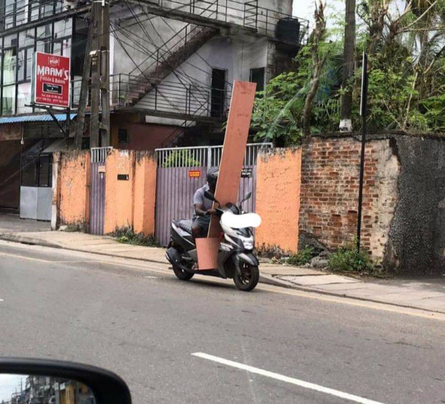 man driving bike while holding a board that blocks his view