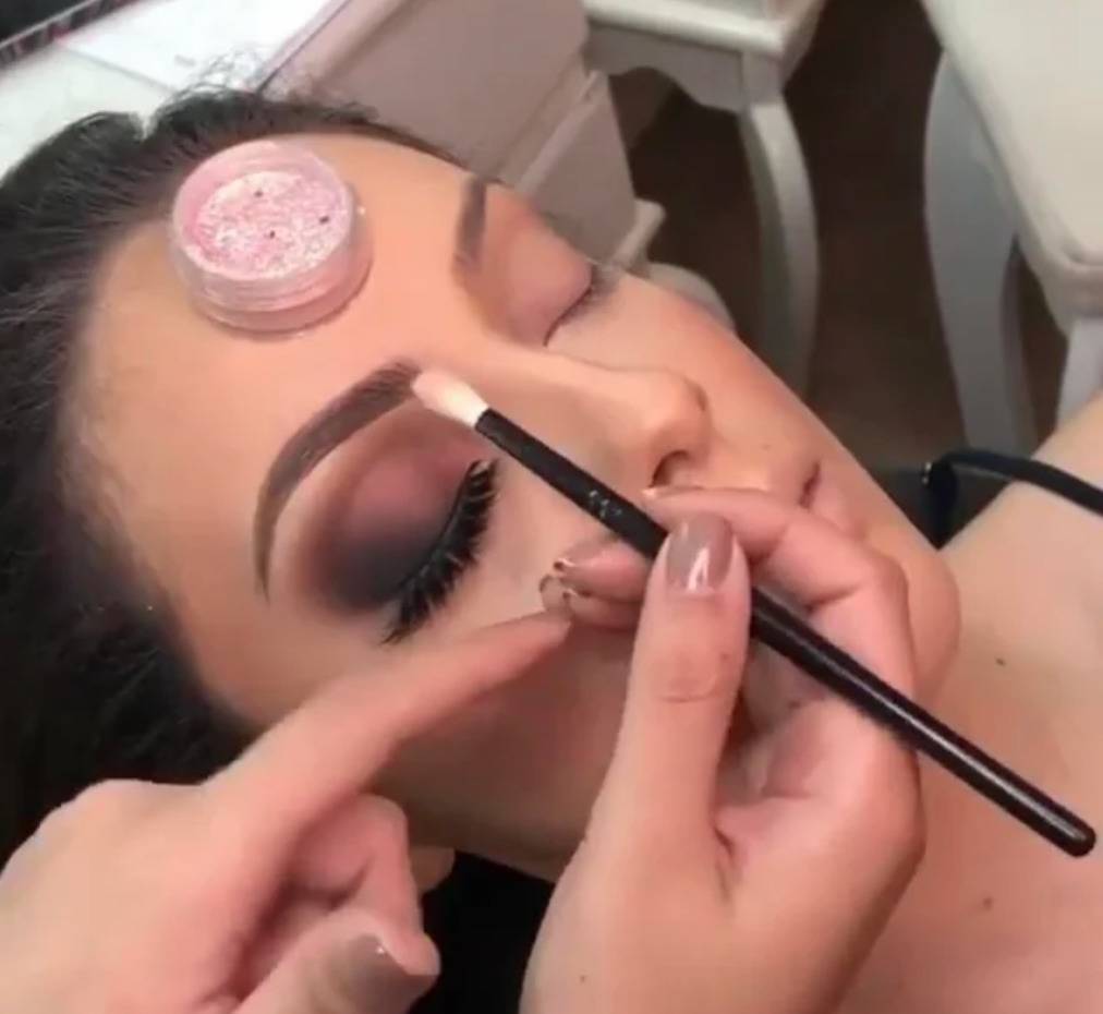 makeup artist is balancing eyeshadow container on client's forehead