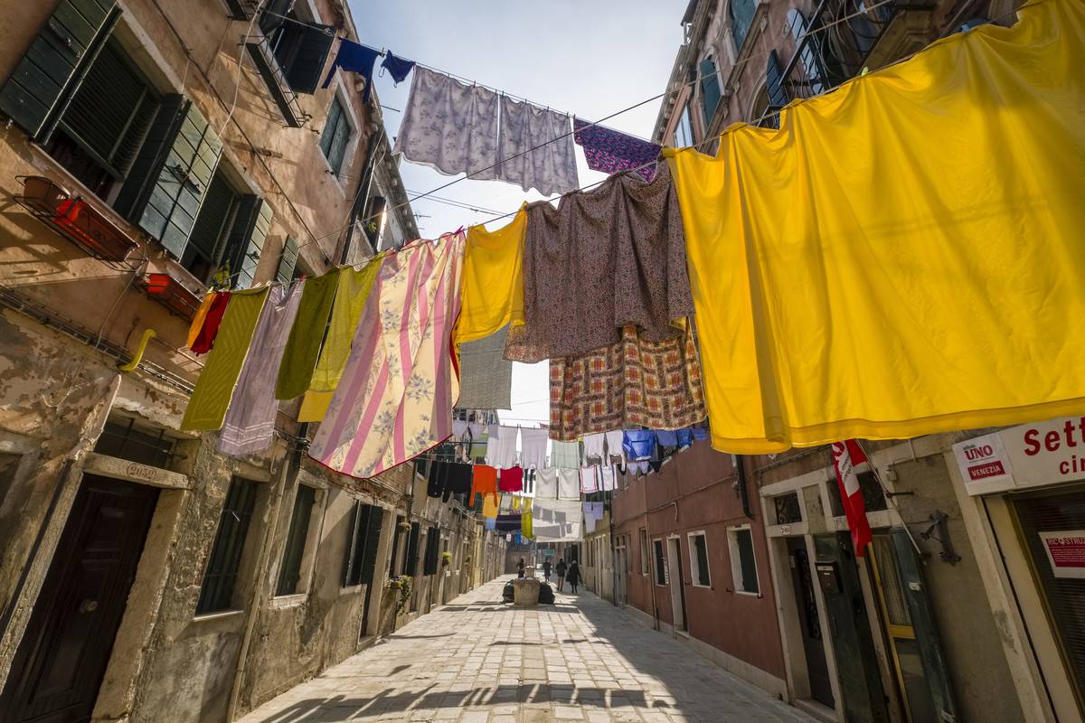 Colorful clothes hang from clotheslines on a narrow street.