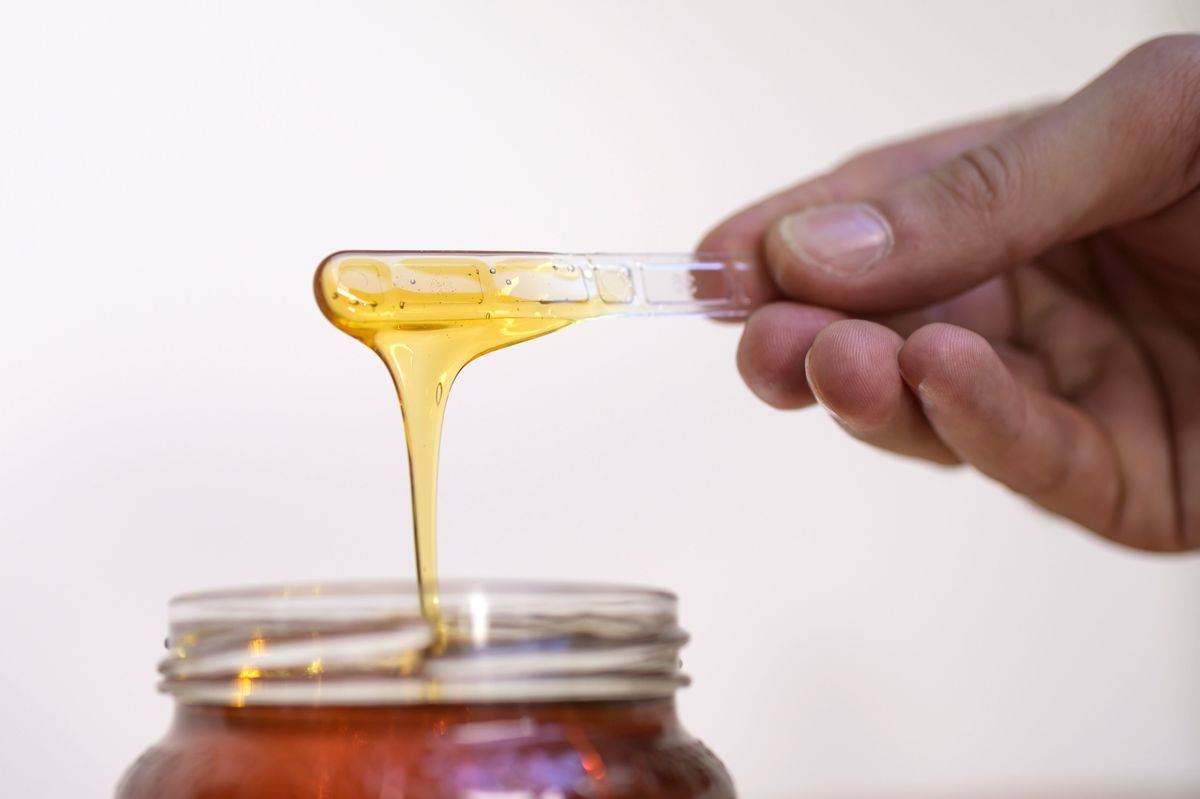 Honey drips from a clear stick into a jar.