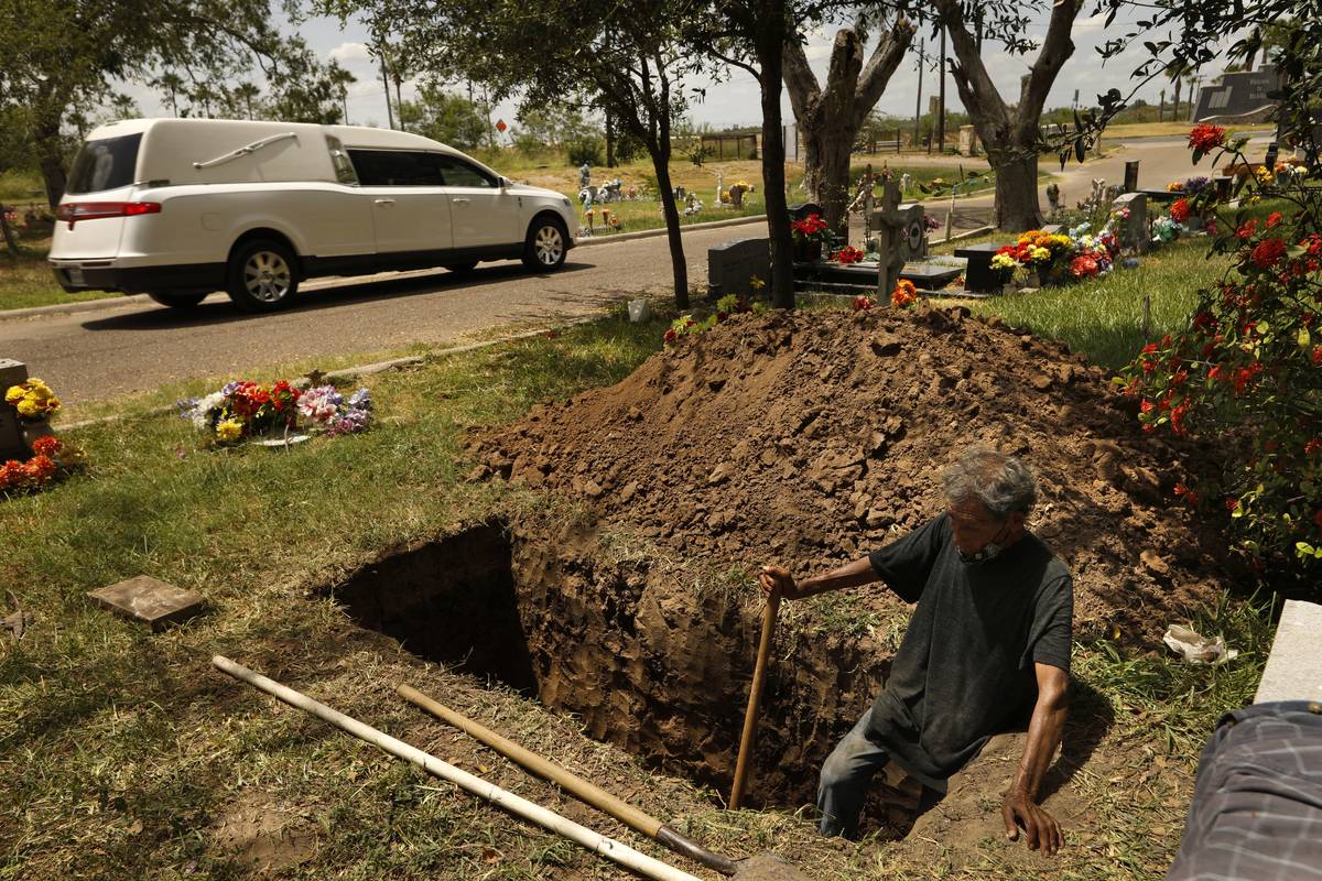 MC ALLEN, TEXAS-July 20, 2020-A hearse passes as Jesus Torres, age 75, digs a grave after the backhoe broke down at La Piedad cemetery in McAllen.