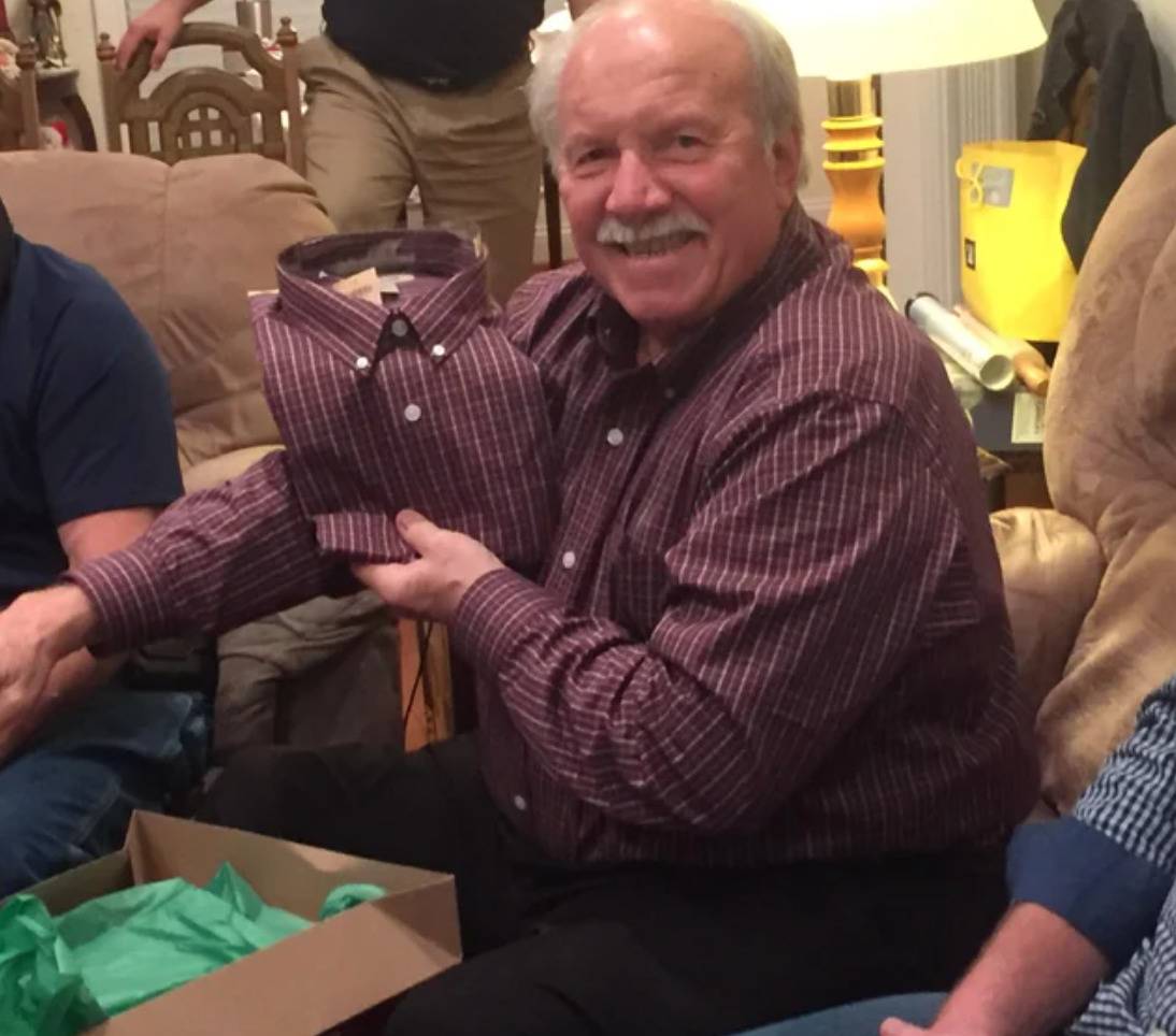 man holding folded new dress shirt that is the same as the one he is wearing