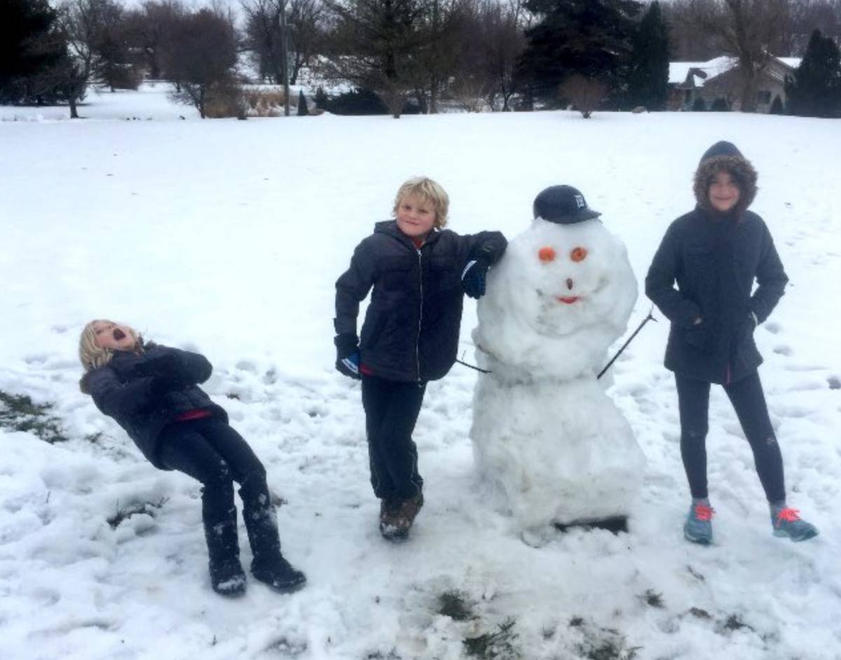 two kids standing by snowman while third is in the process of falling over