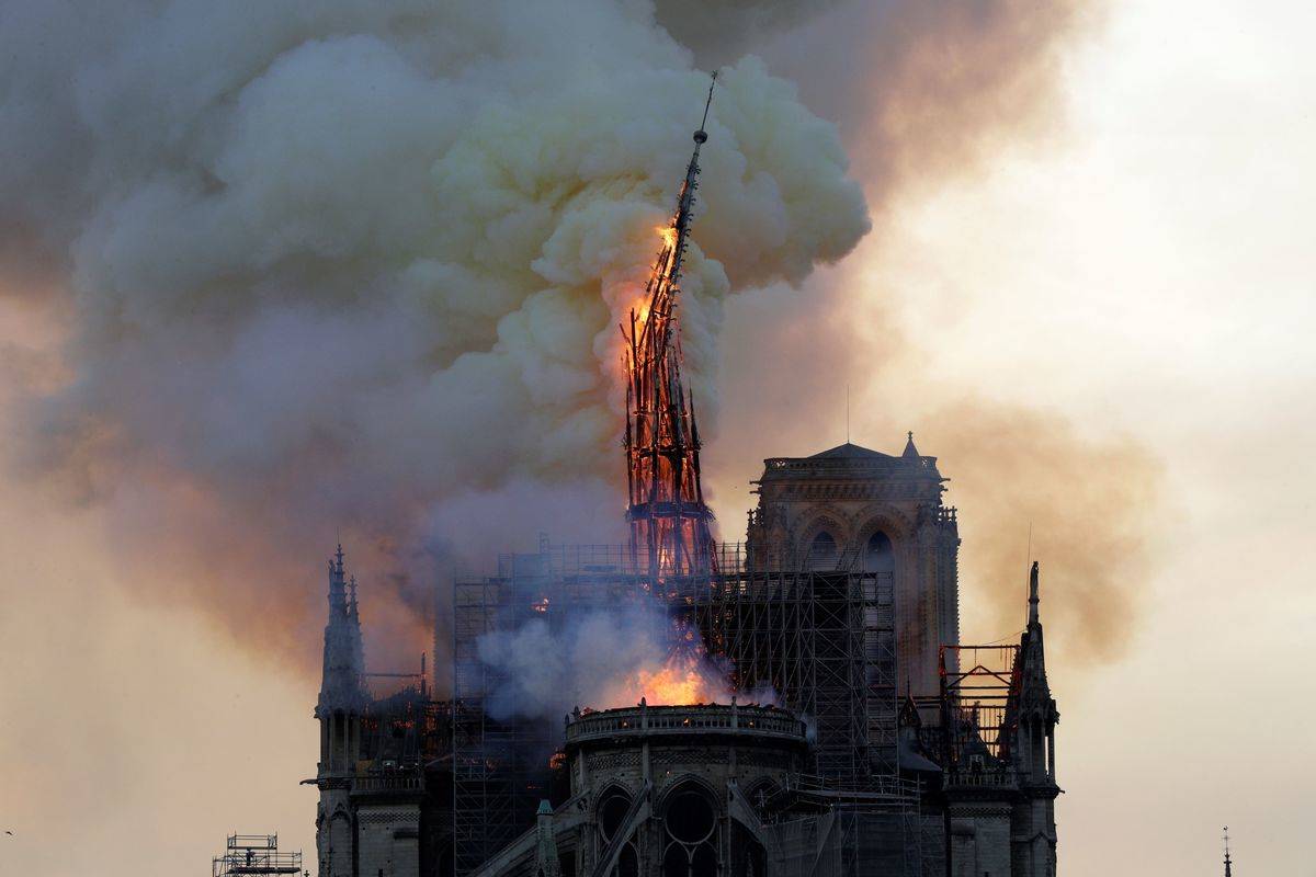 the steeple and spire of the landmark Notre-Dame Cathedral collapses as the cathedral is engulfed in flames in central Paris on April 15, 2019