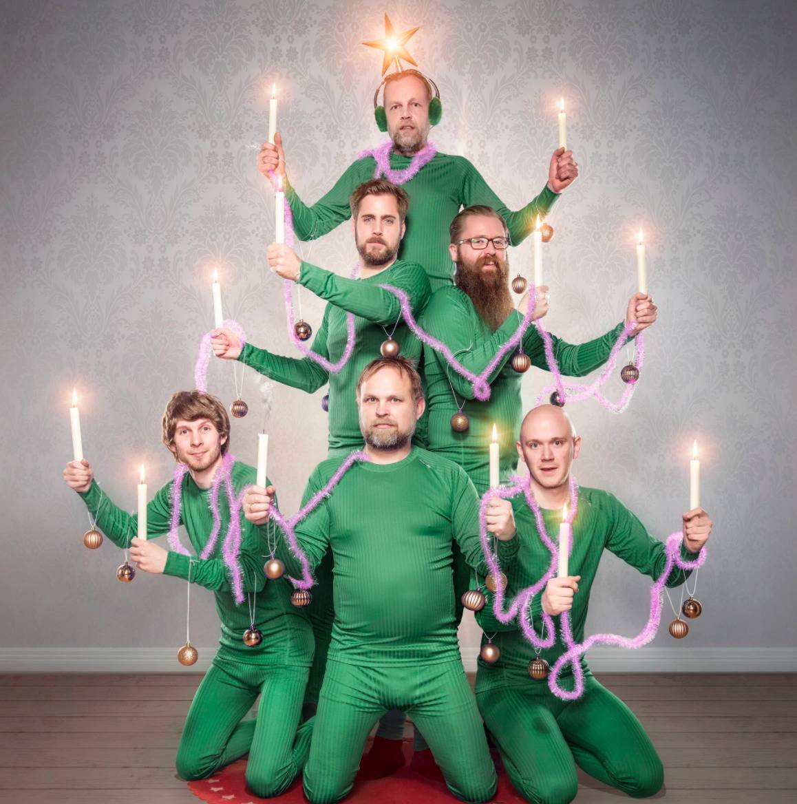 men dressed in all green holding candles and arranged to look like a Christmas tree