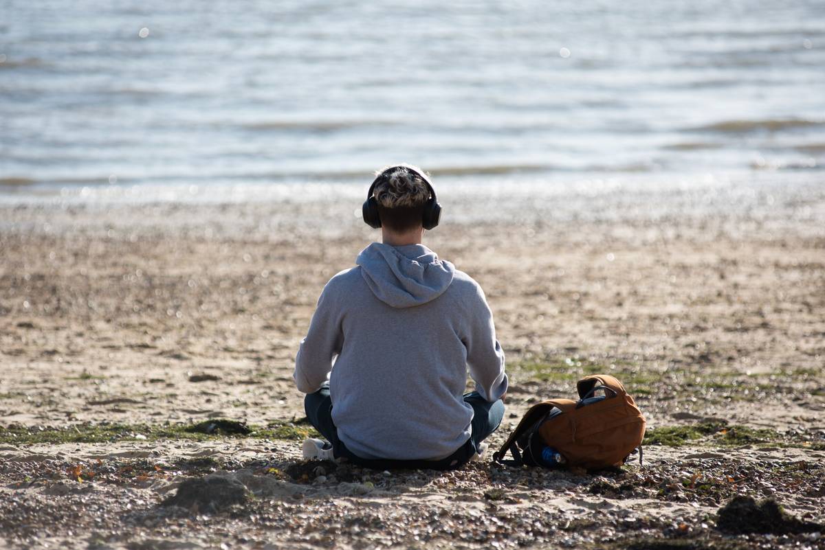 A man sits on the beach with headphones listening to music.