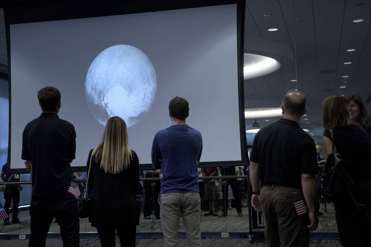People look at an early image of Pluto taken by the New Horizons probe as the craft makes its closest fly-by of the dwarf planet at the Johns Hopkins University Applied Physics Laboratory July 14, 2015 in Laurel, Maryland.