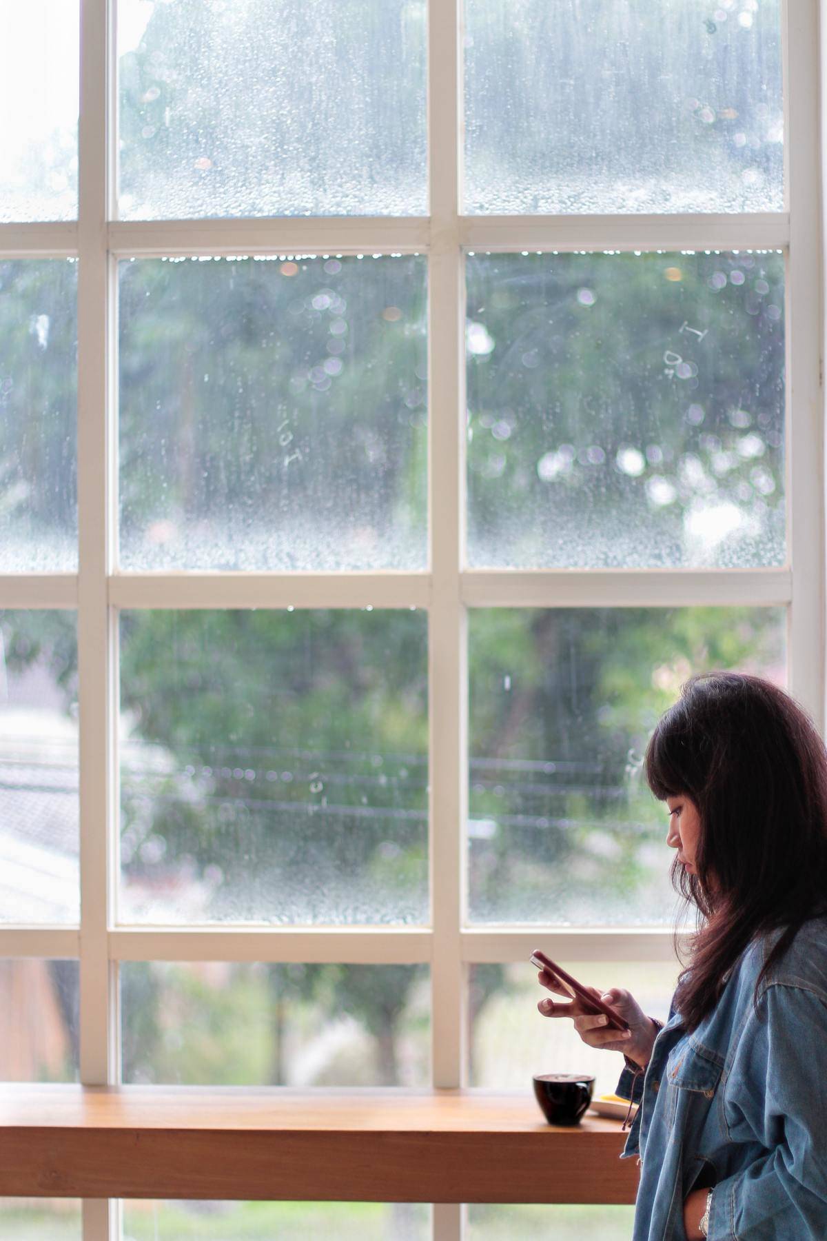 woman sitting in front of a window looking at her phone 