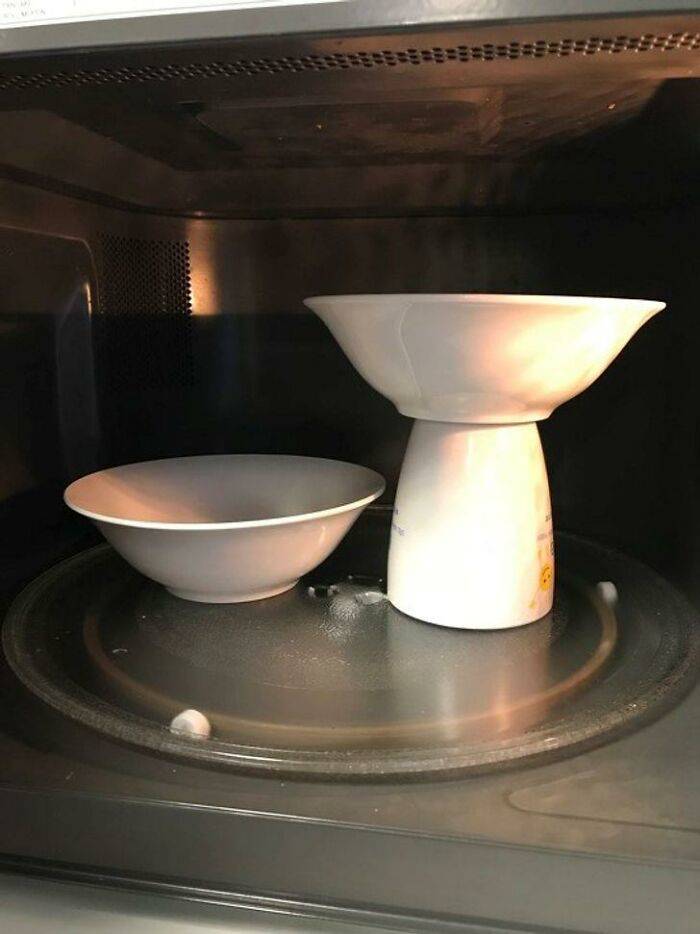 two bowls in microwave, one on top of empty cup to make space