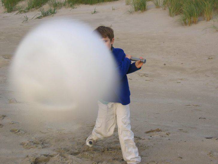 close-up shot of baseball coming towards the camera--child visible in the background with baseball bat