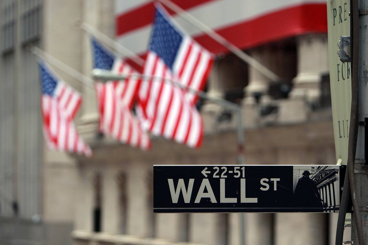 A sign of Wall Street appears in front of American flags.