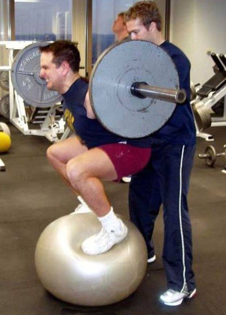 Man standing on yoga ball while lifting weights