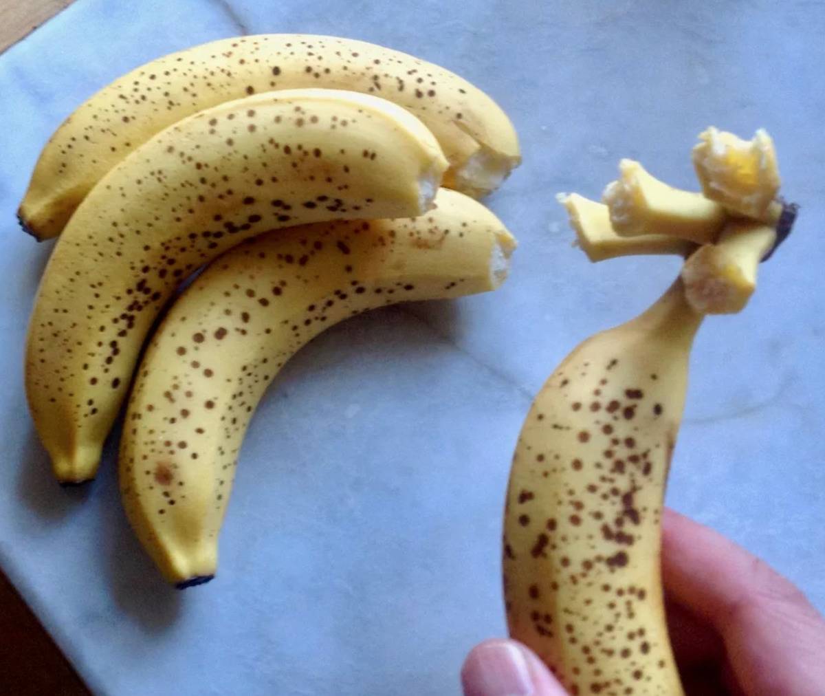person holding single banana with all the stems of the bunch attached and three bananas opened with no stem on them