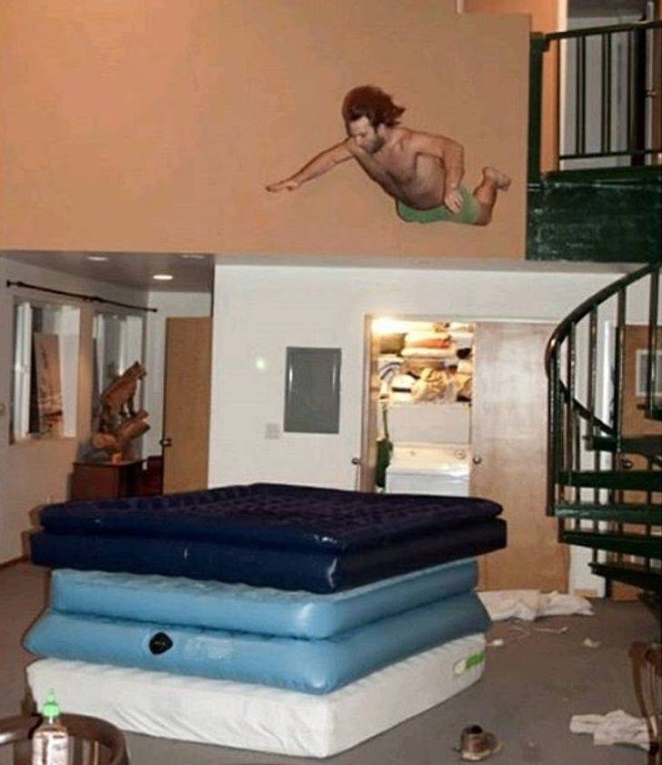 person jumping from balcony onto pile of inflatable mattresses