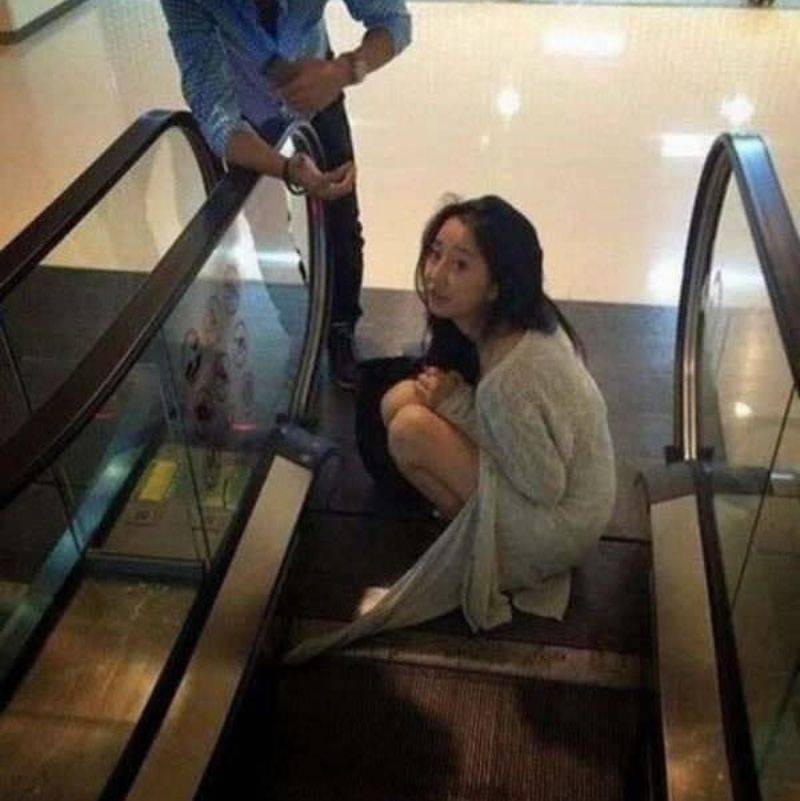 woman kneeling at the bottom of an escalator with her sweater caught in it 