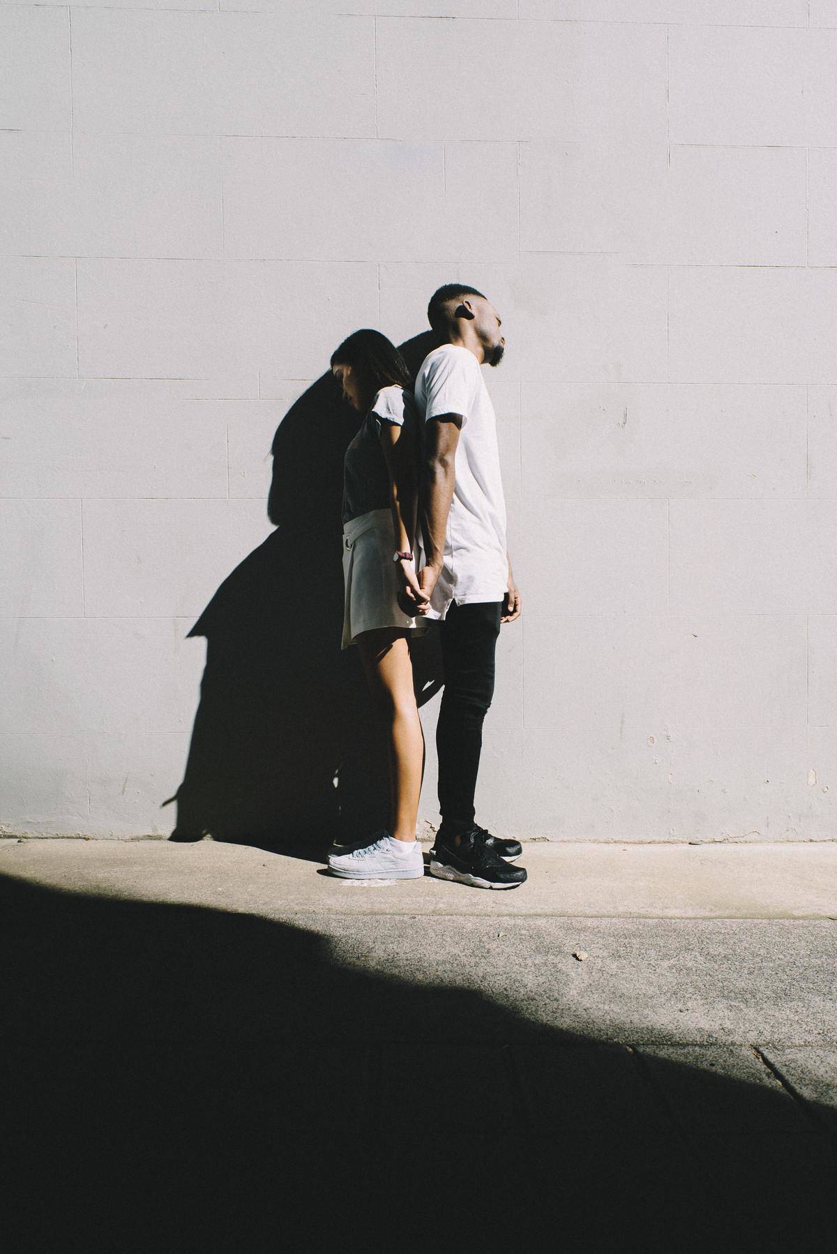couple standing back to back holding hands, but his shadow eclipses her