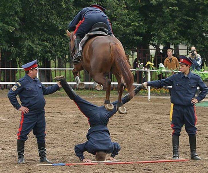 Horse jumping over a man doing the splits while upside down--it looks like the horse might hit him in the family jewels