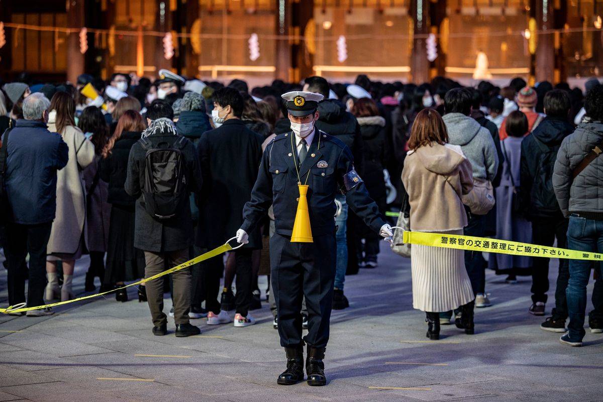 A police officer stands guard as people queue to offer the New Year's prayer at Meiji Shrine on New Year's day in Tokyo on January 1, 2021
