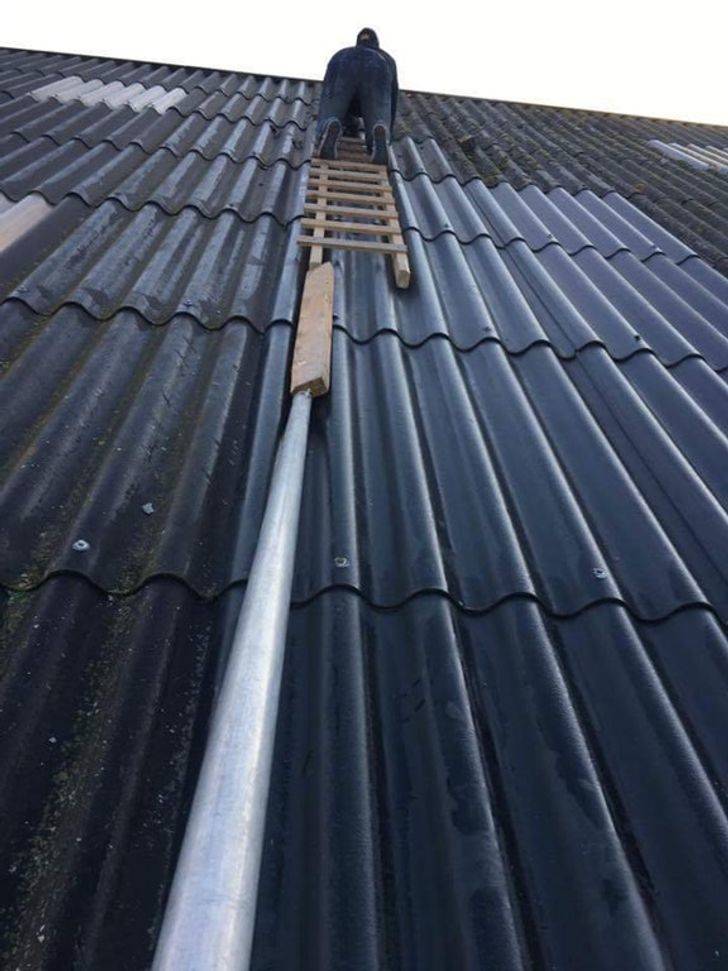 person on roof with ladder balanced on boards and pipes