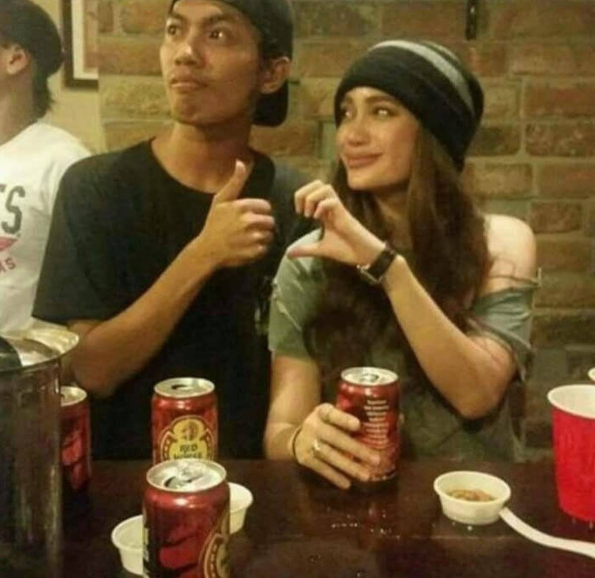 couple taking a picture and one is making half of a heart and the other is making a thumbs up