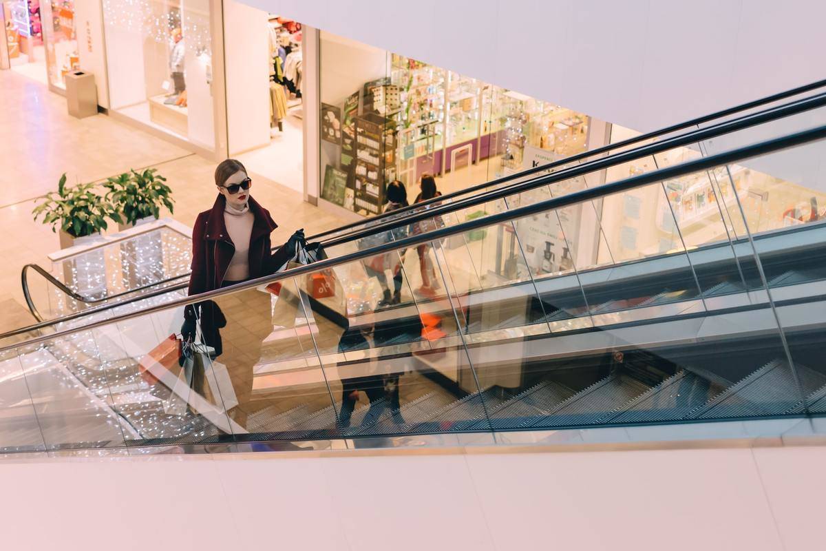 A woman carries shopping bags up an escalator. 