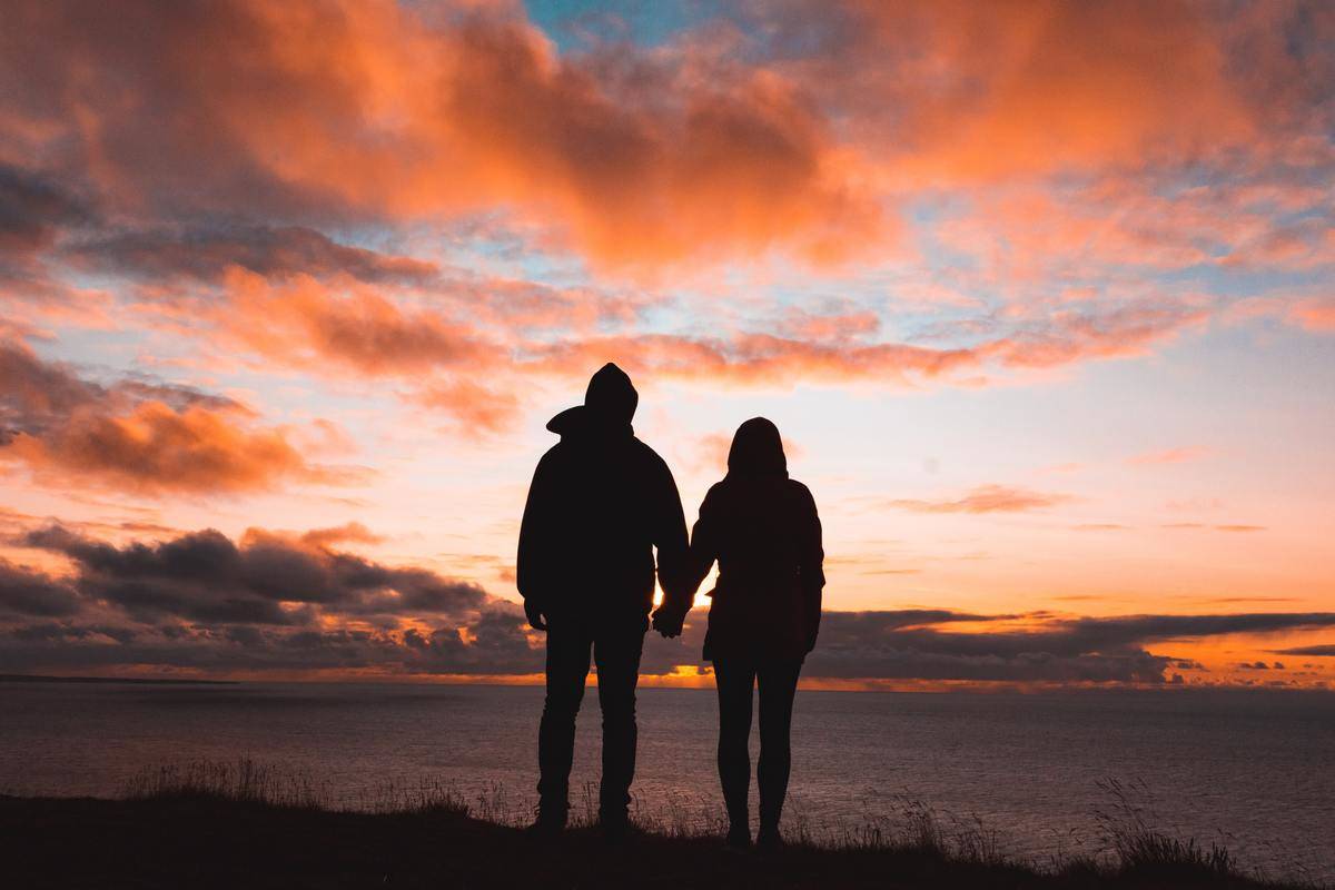silhouette of couple holding hands in front of sunset