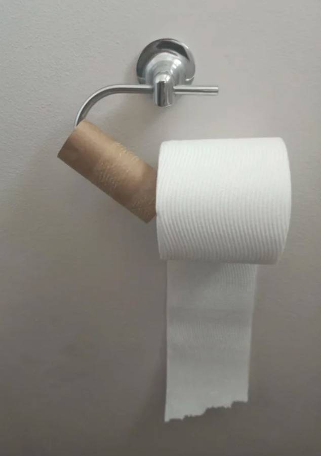 person has shoved new TP roll onto hanging with the old, empty one still on it