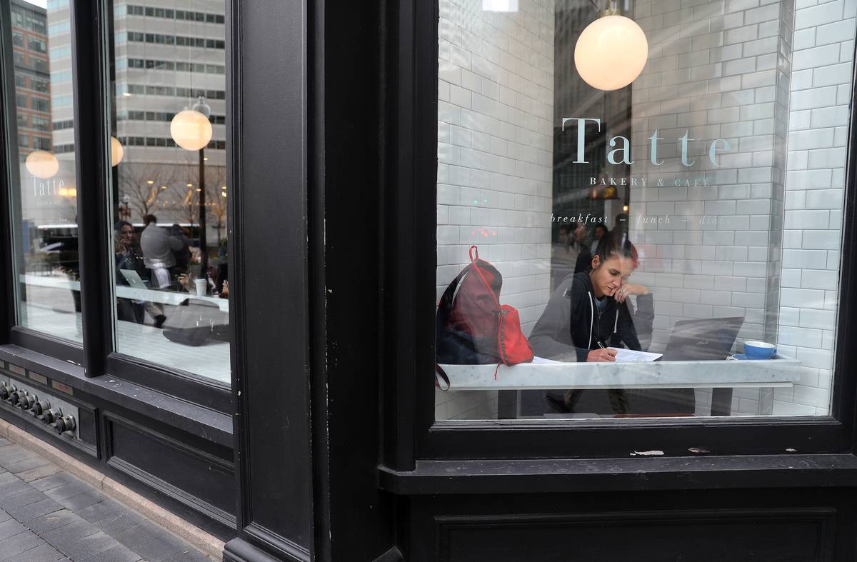 A woman works in front of a coffee shop window.