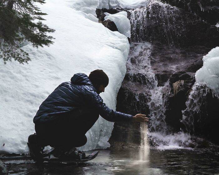 man crouching by frozen waterfall