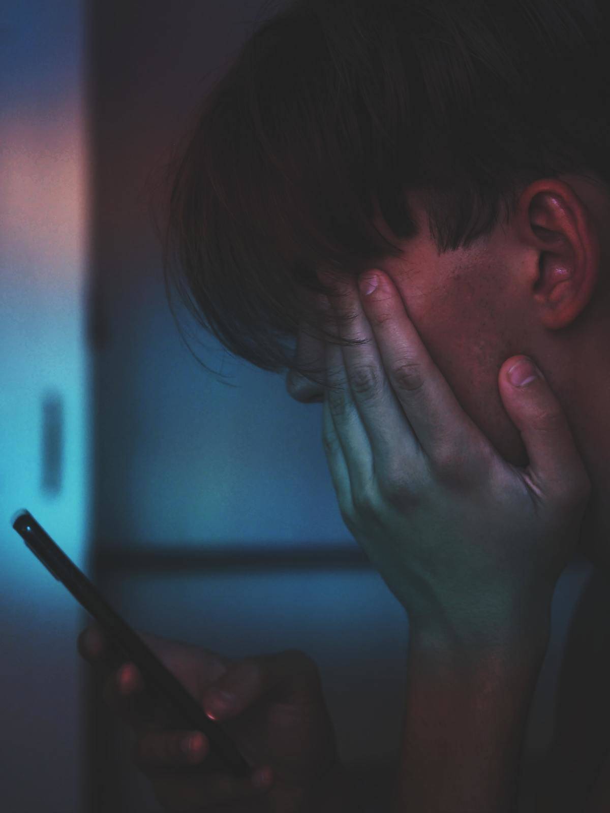 Man looking down at his phone in blue lighting
