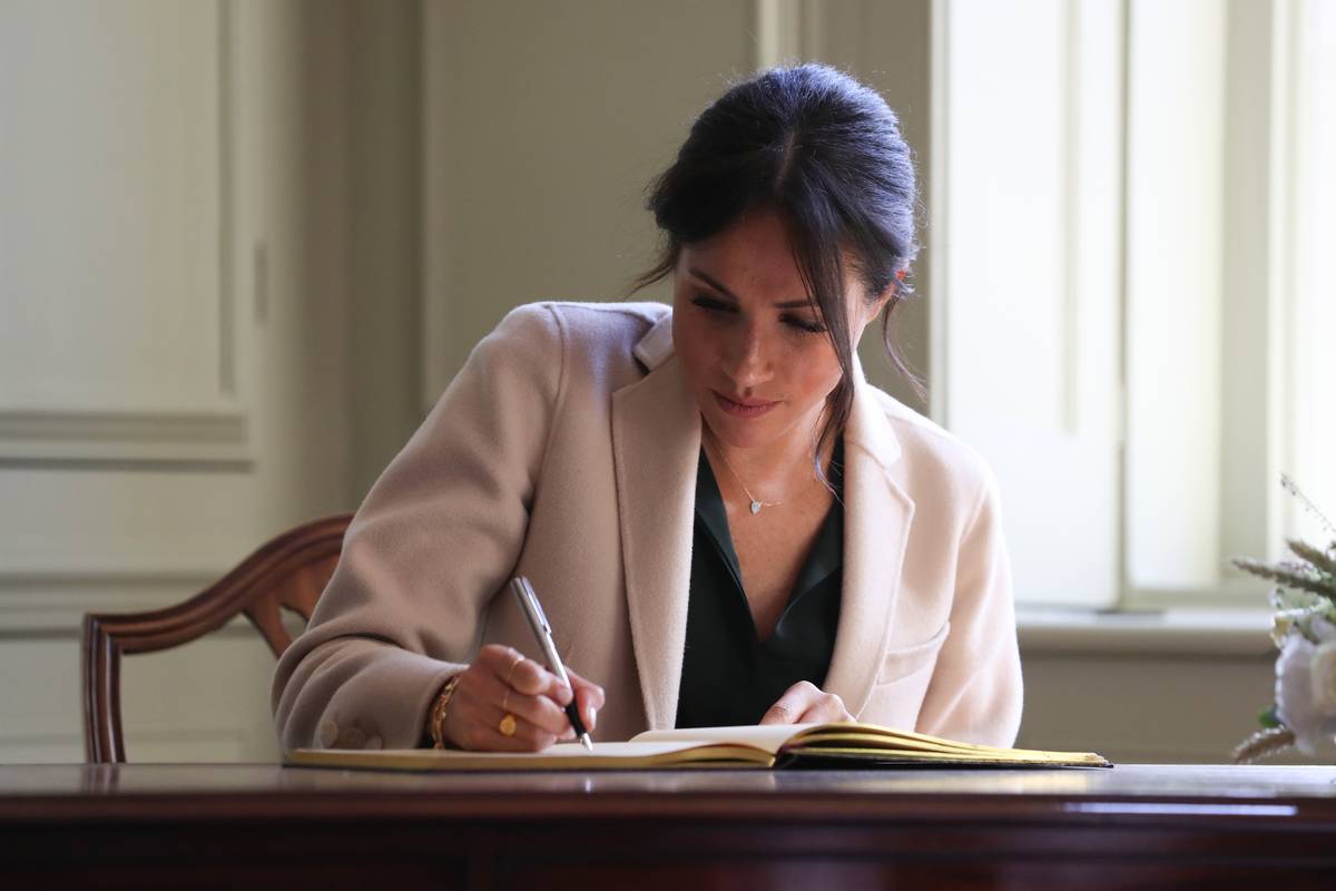 Meghan Markle writes at a desk.