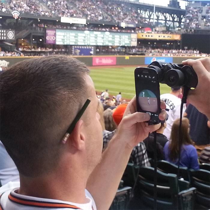 person taking pictures of baseball game using binoculars