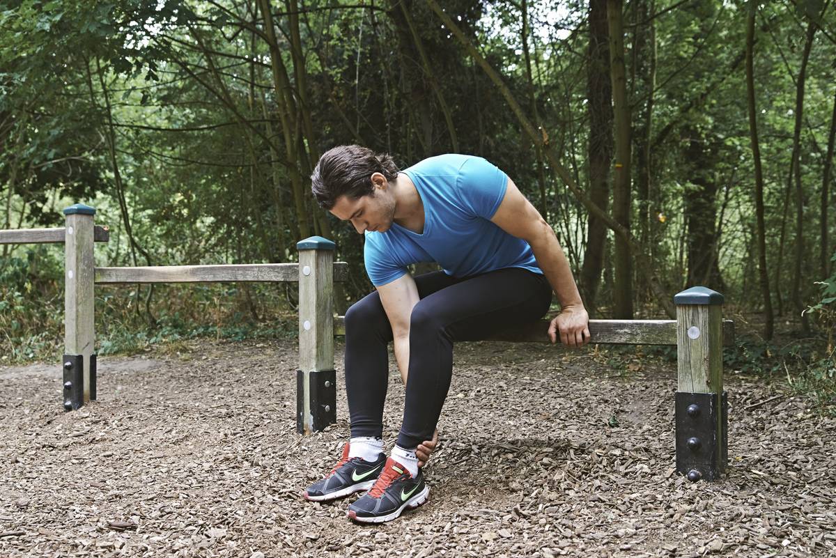 A man sits down and rubs his aching ankle.