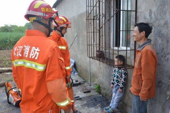 firefighters rescuing little boy who's head is stuck in window grate while dad laughs 